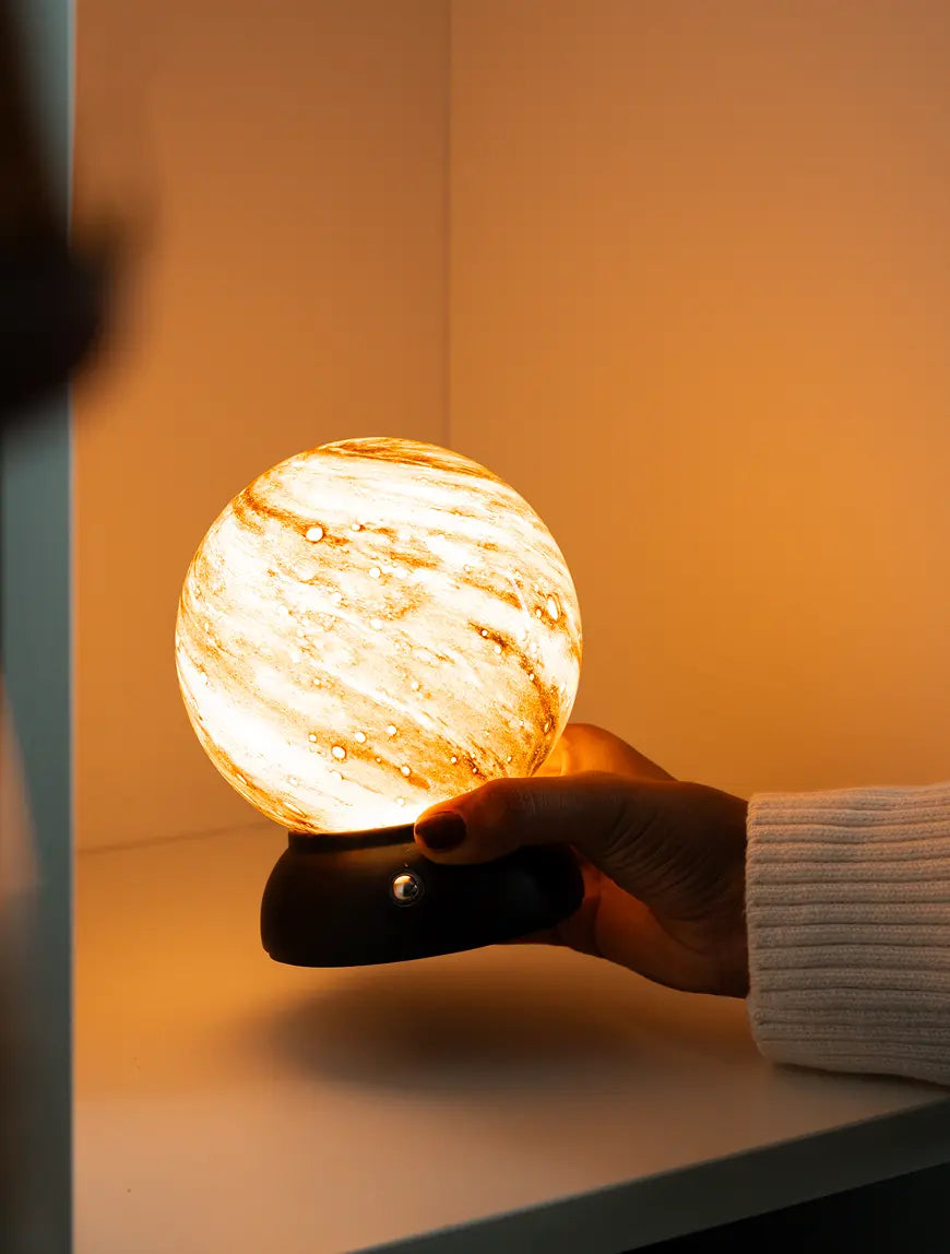 Cordless Cosmo glass table lamp glowing with warm light while held by hand