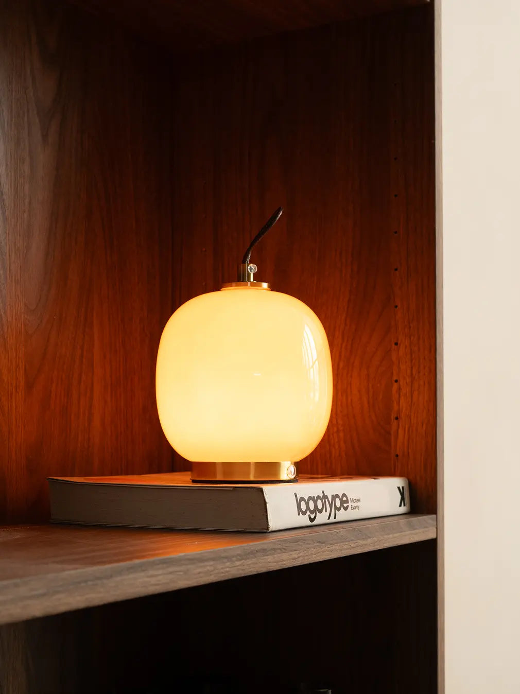Dew rechargeable table lamp glowing with warm light on a wooden shelf