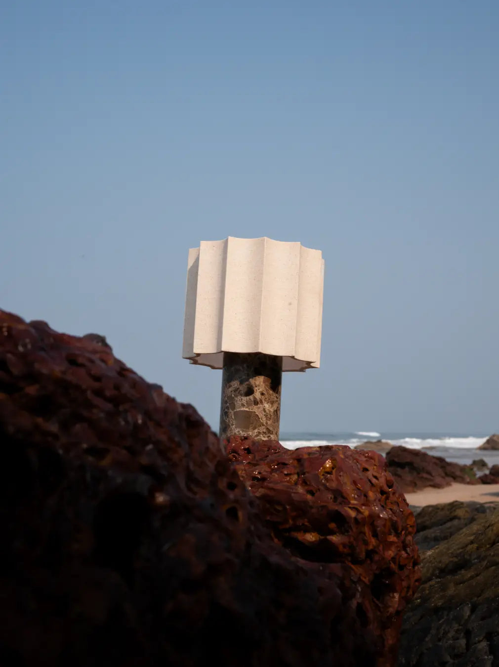 Haze Mocha Marble Portable Table Lamp with scalloped fabric shade on coastal rocks