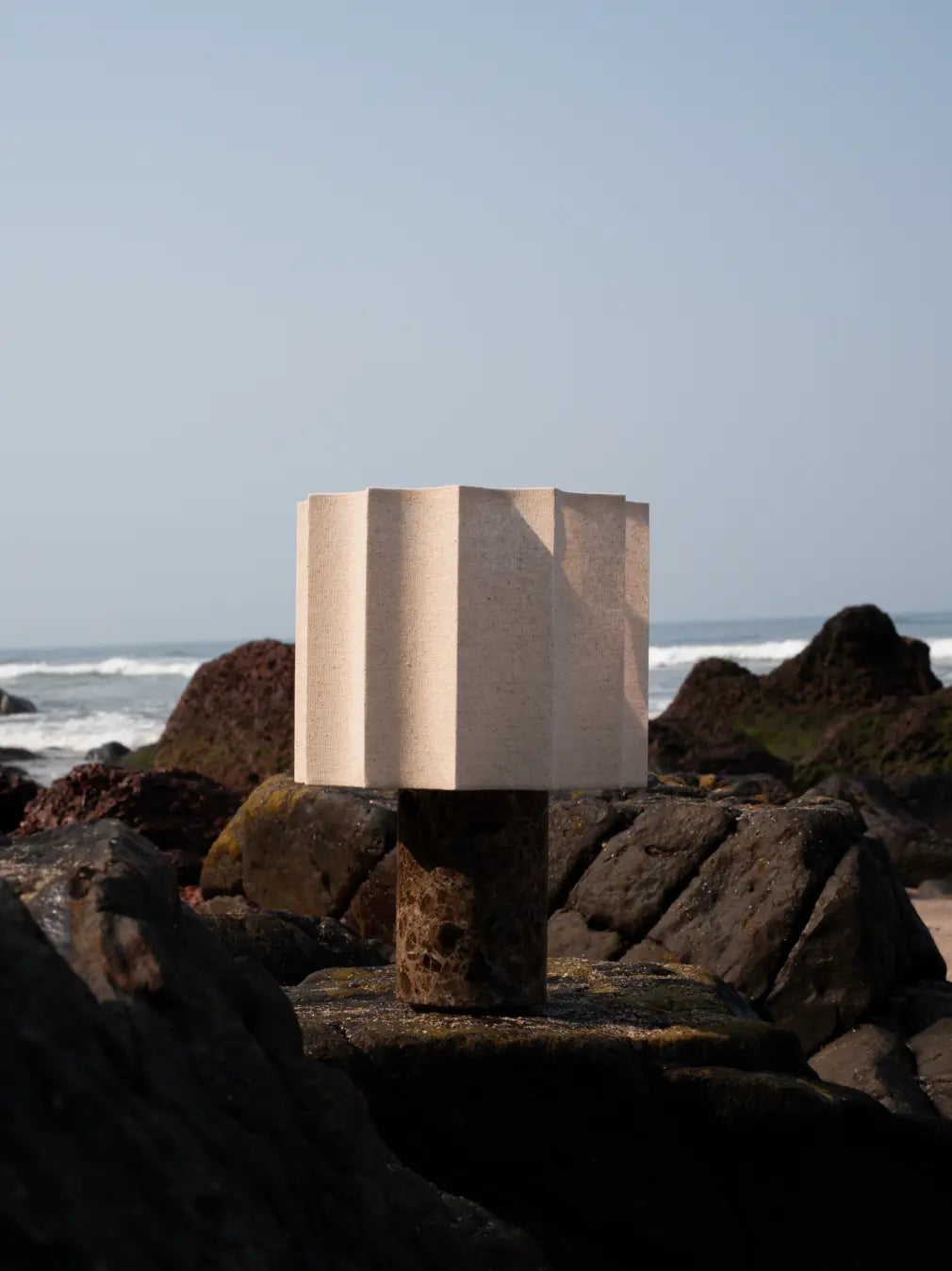 Haze Mocha Marble Portable Table Lamp viewed from the side on rocks beside the sea