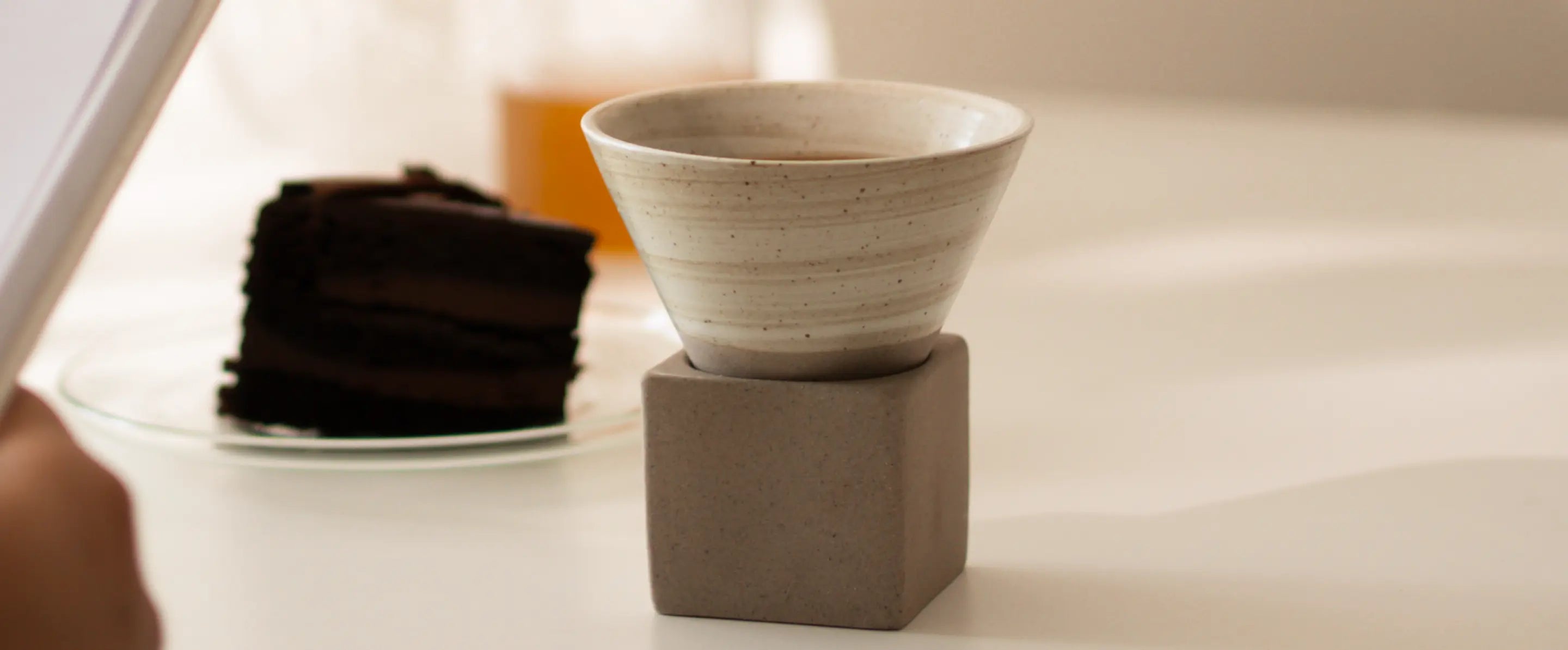 Kono Ceramic Coffee Cup on holder, styled with dessert and book for cozy coffee setting.