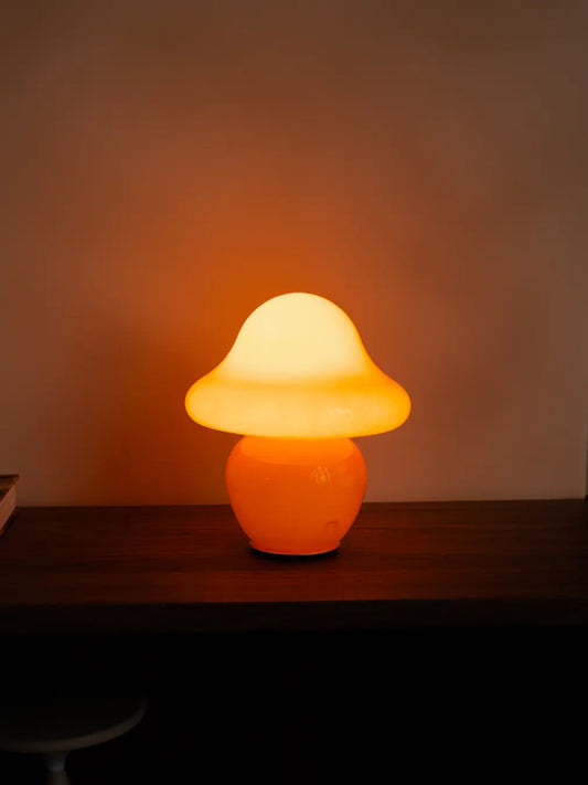 Orange mushroom glass table lamp casting a warm glow against the wall