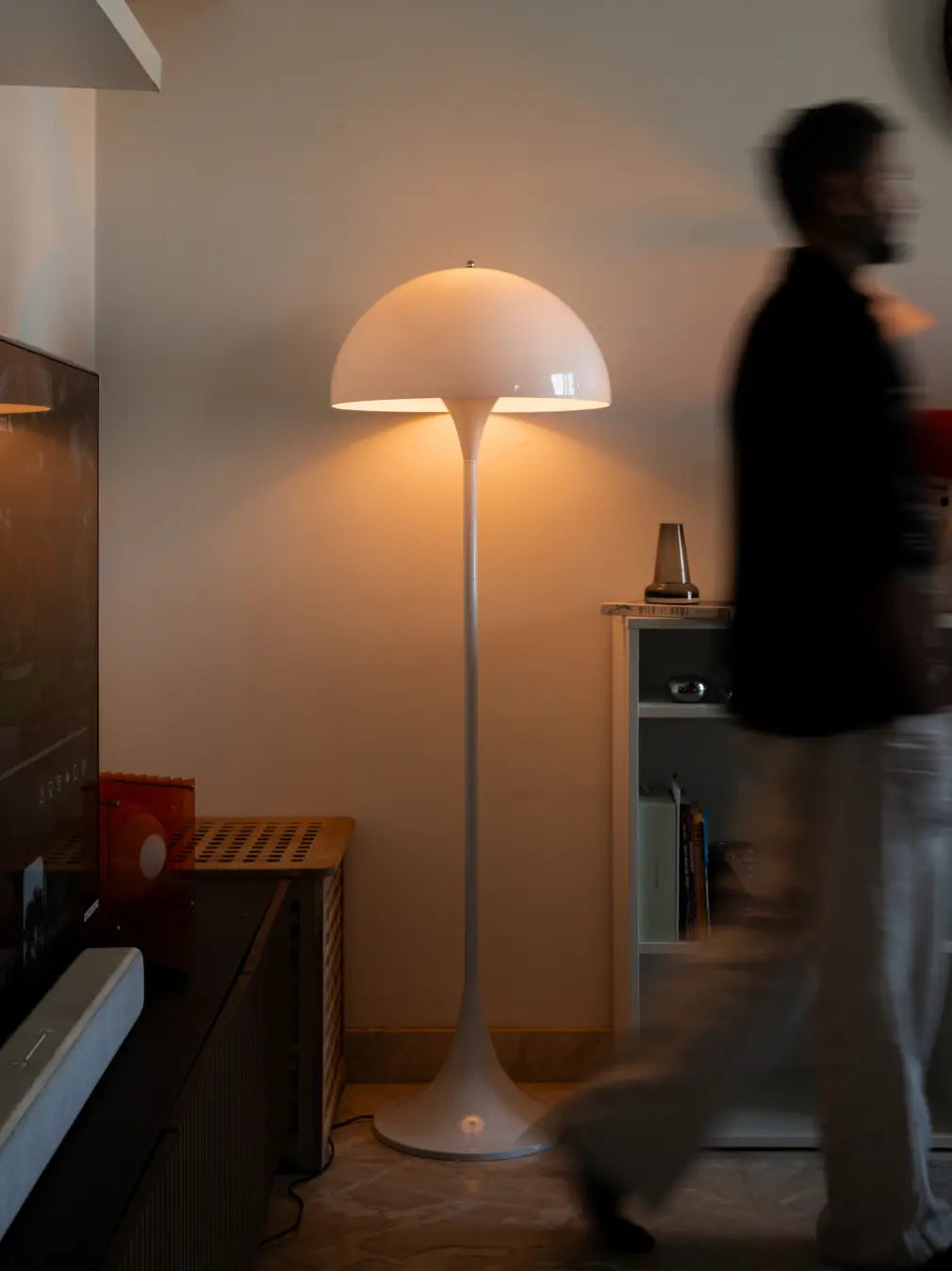 Nova white floor lamp beside a cabinet with a person walking past