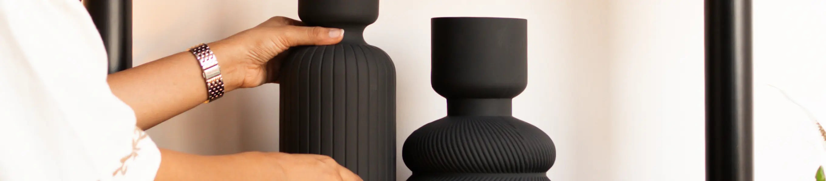 Hands arranging matte black ceramic vases on a shelf in a minimal home setting, highlighting premium home decor accents.