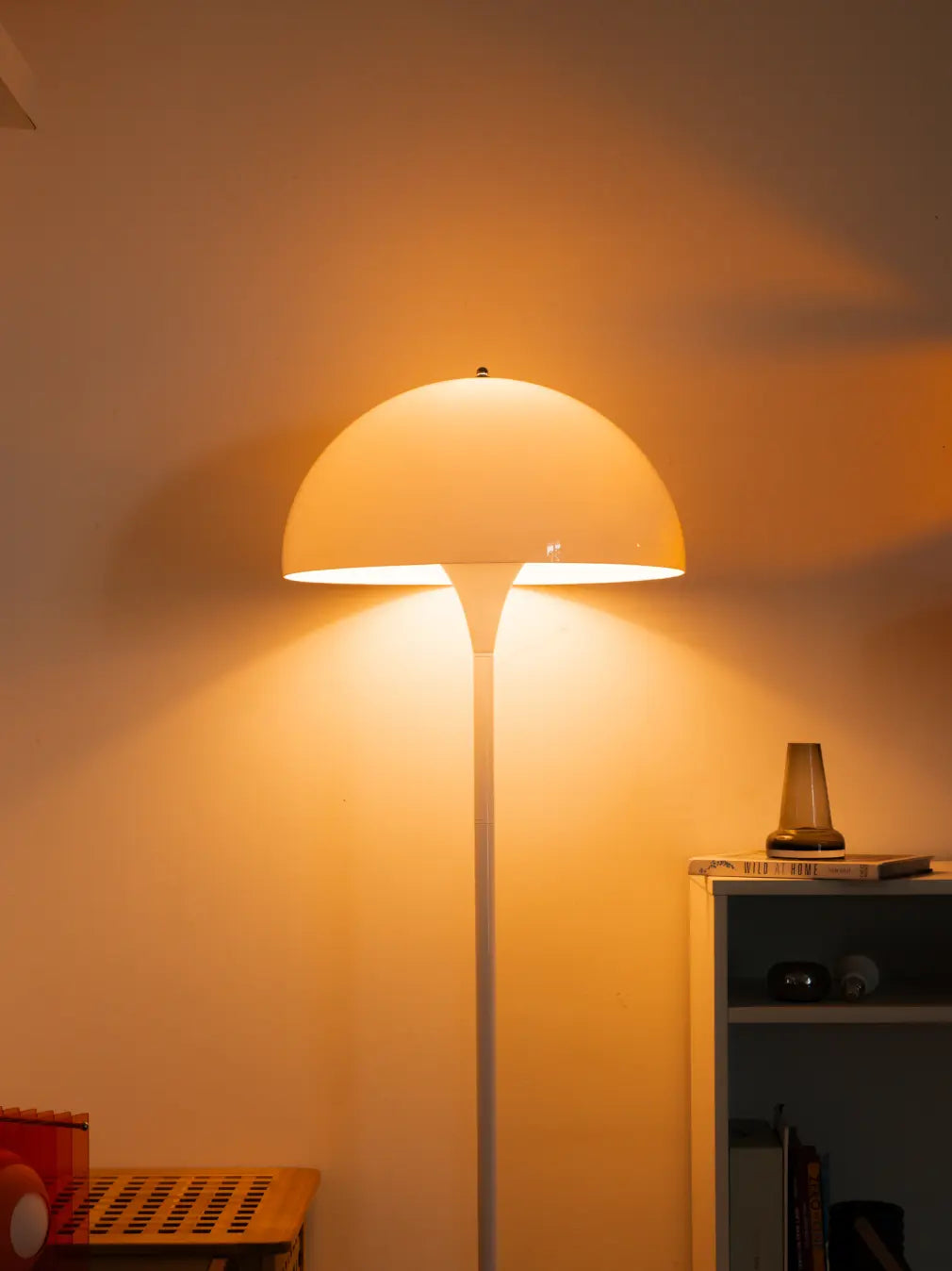 Nova white floor lamp dome shade glowing warmly against a wall