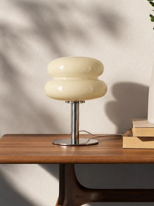 Orbit yellow glass table lamp on a sunlit wooden console beside stacked books.