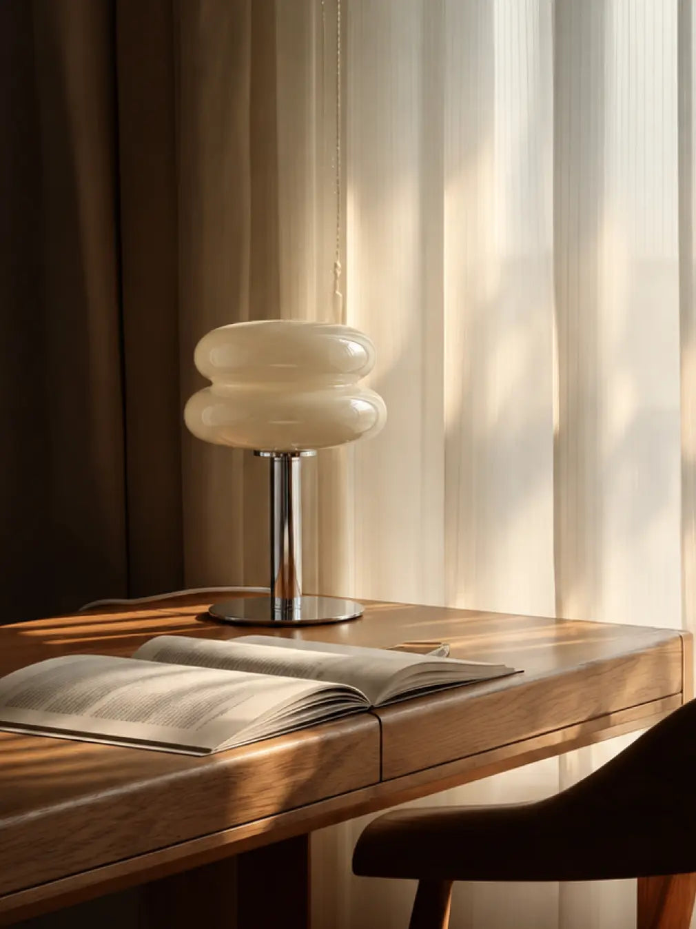 Orbit yellow glass table lamp beside an open book on a wooden desk near a window.