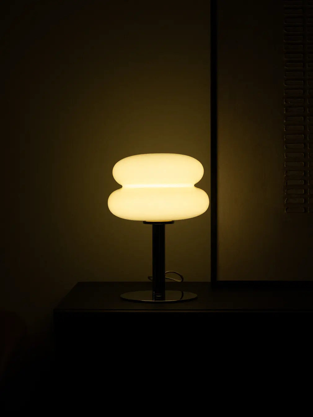 Orbit yellow glass table lamp casting a warm glow on a dark cabinet at night.