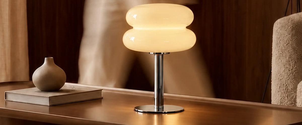 Orbit yellow glass table lamp on a wooden table beside a book and ceramic vase.