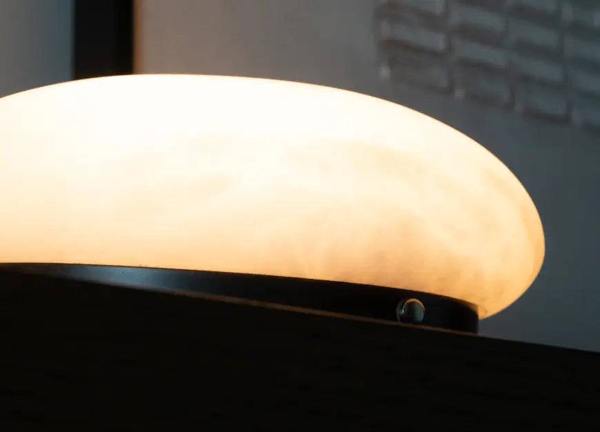 Angled close-up of Pebble Marble Portable Table Lamp with lit shade and slim black base