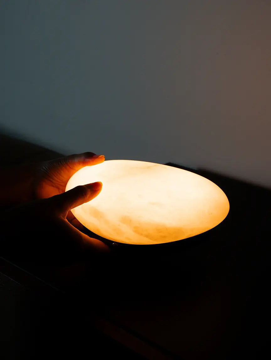 Hands holding the glowing marble shade of the Pebble Marble Portable Table Lamp