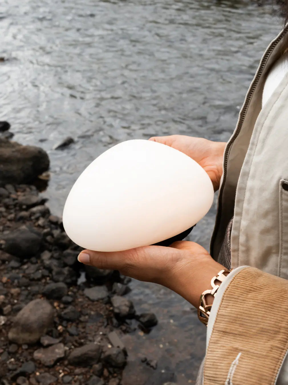 White Pebble Marble Portable Table Lamp held in two hands beside a stream
